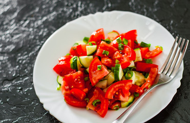 fresh vegetable salad with tomato, cucumber and green onion in white plate on black background.