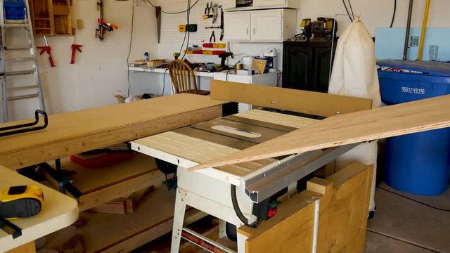 Two men rip cut a half sheet of plywood on a table saw