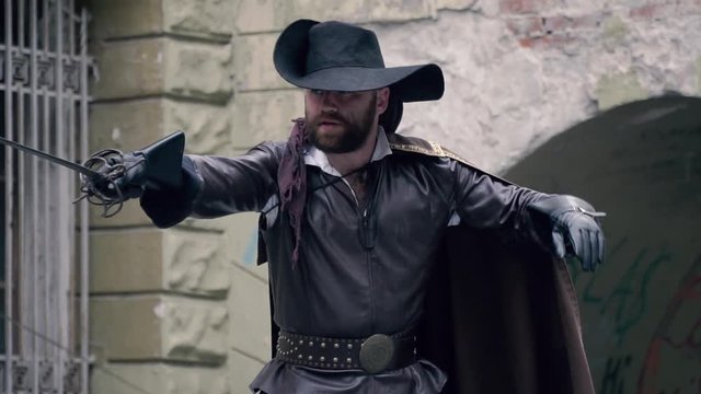 Musketeer in leather clothes and a black hat preparing for battle, slow motion
