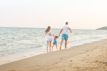 Close up Happy family of three - beatiful wife, father and daughter having fun walking on beach at sunset. Family traveling concept.