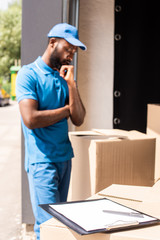 african american delivery man looking at boxes with clipboard and pen on foreground