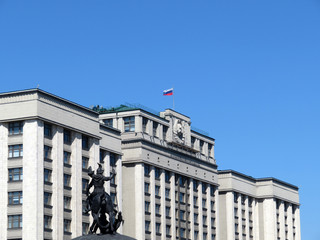 Fototapeta na wymiar Russian flag on the Parliament building in Moscow against clear blue sky. State Duma and Statue of St. George the victorious