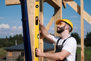 The man is a builder on the roof of a wooden frame house.