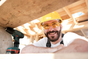 The man is a builder on the roof of a wooden frame house.