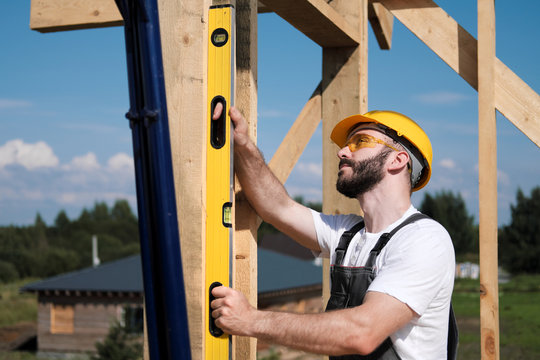 The man is a builder on the roof of a wooden frame house.