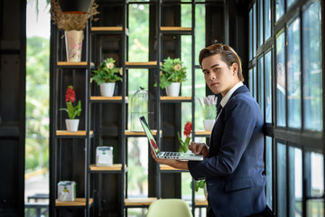 Businessmen are using a laptop computer standing near the window glass. Within the office. Technology and Business Communication Concept