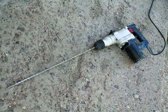 perforator with a long drill rests on a concrete surface