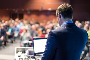 Speaker giving a talk on corporate business conference. Unrecognizable people in audience at...