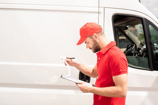 side view of caucasian delivery man looking at clipboard near van