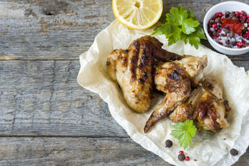 Chicken wings baked on grill with fresh herbs, lemon on wooden background.