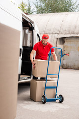 young delivery man discharging cardboard boxes from van