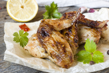 Chicken wings baked on grill with fresh herbs, lemon on wooden background.