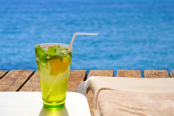 Cold mojito drink and sun bed on the wooden beach pier. Summer vacation concept image.