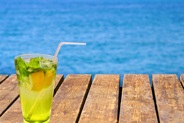 Cold mojito drink on the wooden beach pier. Summer vacation concept image.