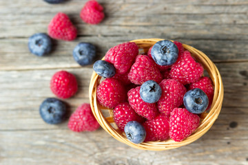 Raspberries and blueberries in a basket on a wooden table.