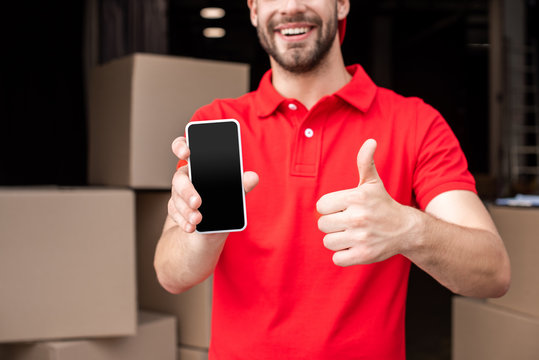 cropped shot of cheerful delivery man with smartphone showing thumb up