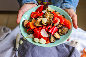 Woman hands holds roasted grilled vegetables (Ratatouille) with eggplant, red pepper, onion,...