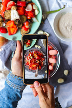 Woman hands takes smartphone food photo of fresh tomatoes salad for lunch. Makes food photography for social networks or blogging with phone. Raw, vegan, vegetarian food