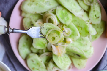 Woman hands tastes with fork green fresh cucumber salad with onion rings spices, herbs, garlic and unrefined oil. Raw vegan lunch, vegetarian healthy dinner