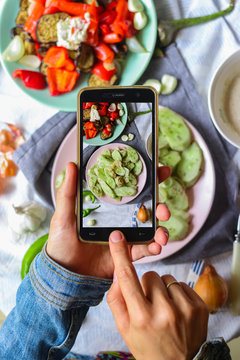 Woman hands takes smartphone food photo of cucumber salad for lunch. Makes food photography for social networks or blogging with phone. Raw, vegan, vegetarian food