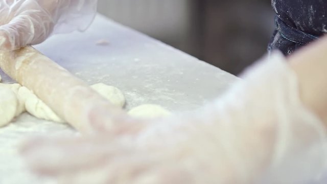 Close-up shot of hands of professional baker rolling dough on floury table and putting small disks in a row