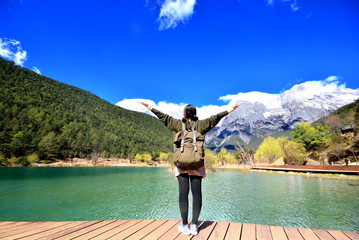 back of girl travel alone stand in front of extremely blue river ,Blue Moon valley, Jade Dragon Snow Mountain seen from a distance, Lijiang, China