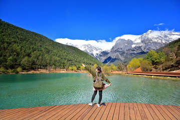 back of girl travel alone stand in front of extremely blue river ,Blue Moon valley, Jade Dragon Snow Mountain seen from a distance, Lijiang, China