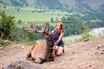 A young red-haired woman dressed in sports clothes stroking the horns and skin of a deer maral
