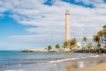 Fototapeta premium Tenerife, Canarias islands/ Spain - July 22, 2018: View of empty beach of tourists and high lighthouse on Canarias, view of bay with palms. Blue Atlantic ocean and beach on Gran Canaria.