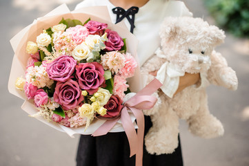 School girl dressed in school uniform holding a bright colorful festive bouquet and teddy bear