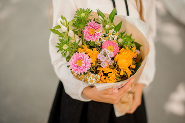School girl holding a bright festive bouquet of pink, yellow and green flowers