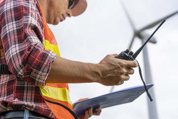 Senior electric engineer with safery helmet workingat wind mill or wind turbine power generator  station with tablet or clipboard..Clean energy concept.