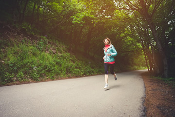 Fototapeta premium Young fitness blonde woman in headphones running at morning caucasian forest trail in sun light