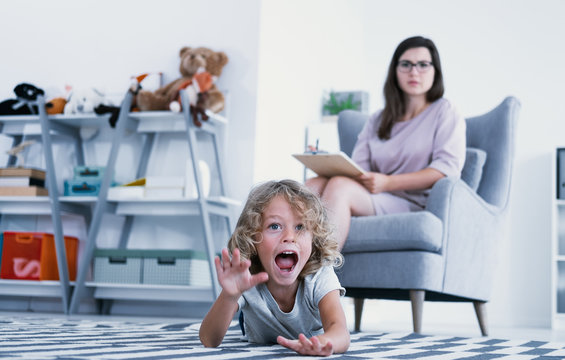 An overactive child screaming and hitting a floor while a psychotherapist is making a diagnose during a meeting in a family support center.