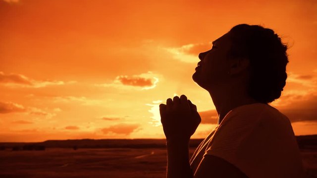 the girl prays. Girl folded her hands in prayer silhouette at lifestyle sunset. slow motion video. Girl folded her hands in prayer pray to God. girl praying asks forgiveness for sins of repentance