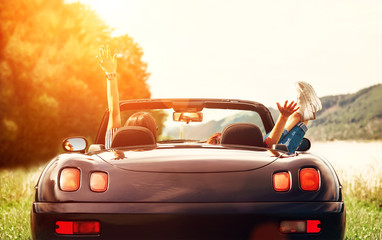 Two girls travelers sit in cabriolet car and enjoy with beautiful view - obrazy, fototapety, plakaty