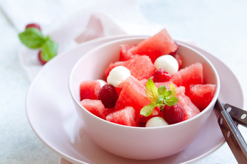 Watermelon salad with raspberry and mozzarella in pink bowl on white table