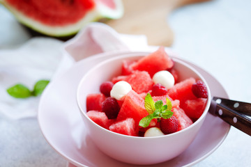 Watermelon salad with raspberry and mozzarella in pink bowl on white table