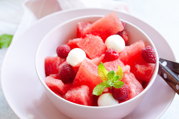 Watermelon salad with raspberry and mozzarella in pink bowl on white table