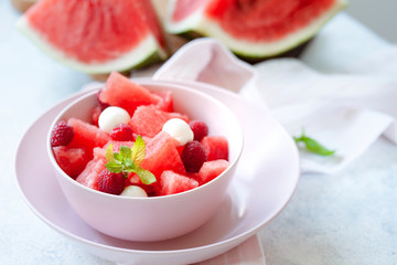 Watermelon salad with raspberry and mozzarella in pink bowl on white table