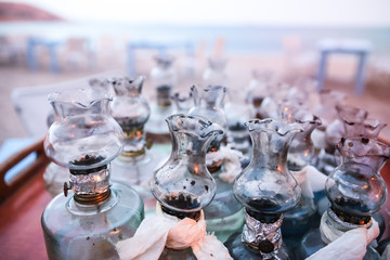 Old Oil Glass Lamps with DIY fixes gathered on Table on Greek Beach at Sunset.