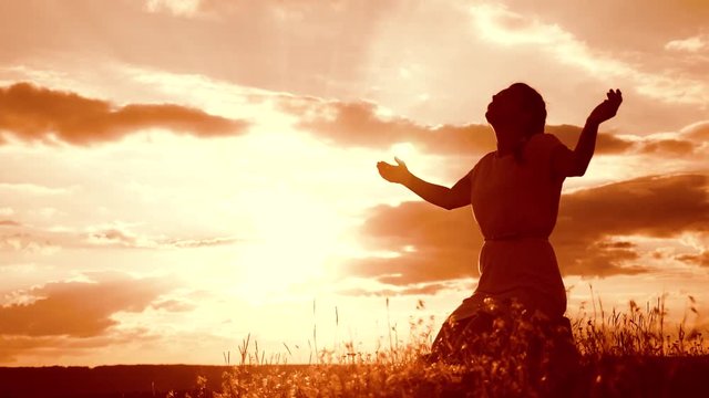 Girl folded her hands in prayer silhouette at sunset. woman praying on her knees. slow motion video. concept Christianity religion catholicism. Girl folded her hands in prayer pray to God. the girl