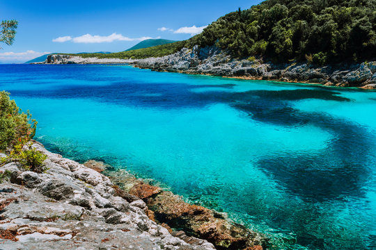Rocky coastline near Dafnoudi beach in Kefalonia, Greece. Isolated bay with pure crystal clean turquoise sea water surrounded by cypress trees. Dark pattern on lagoon bottom - Powered by Adobe