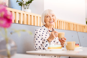 Morning with coffee. Low angle of beautiful senior woman relishing coffee and smiling to camera