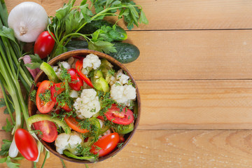 Fresh salad of cauliflower with tomatoes, broccoli, olives, sweet pepper, herbs and vegetables in a bowl on a wooden table. Top view. Copy space. Close-up