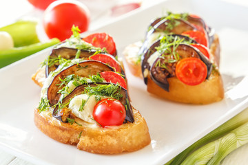 Bruschetta with fried eggplants, fresh tomatoes and mozzarella cheese in a white plate. Close-up