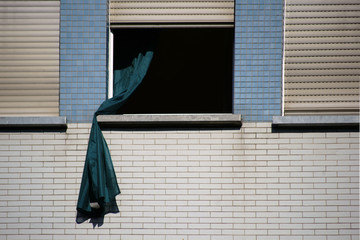 Gardine weht aus dem Fenster / Eine lose Gardine weht aus dem Fenster eines verklinkerten...