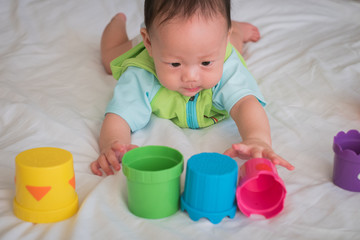 The Asian pretty boy enjoy playing toys, cups, on the bed.