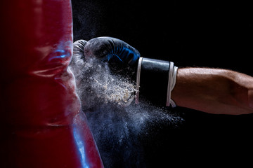 Close-up hand of boxer at the moment of impact on punching bag over black background - obrazy, fototapety, plakaty