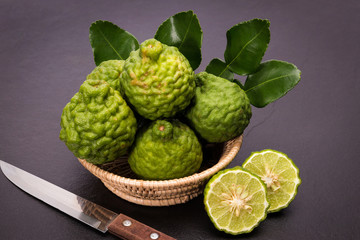 Obraz premium Bergamot, kaffir lime and kaffir lime leaf with basket and knife on dark background